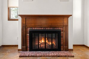 A fireplace with a brick surround and a black glass screen, set in a room with white walls and a tiled floor. - Spacious 7BR Brooklyn Center Home for 14 (Minneapolis)
