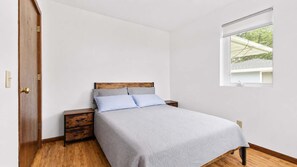 A bedroom with a bed, a nightstand, a wooden wardrobe, and a window with a view. - Spacious 7BR Brooklyn Center Home for 14 (Minneapolis)