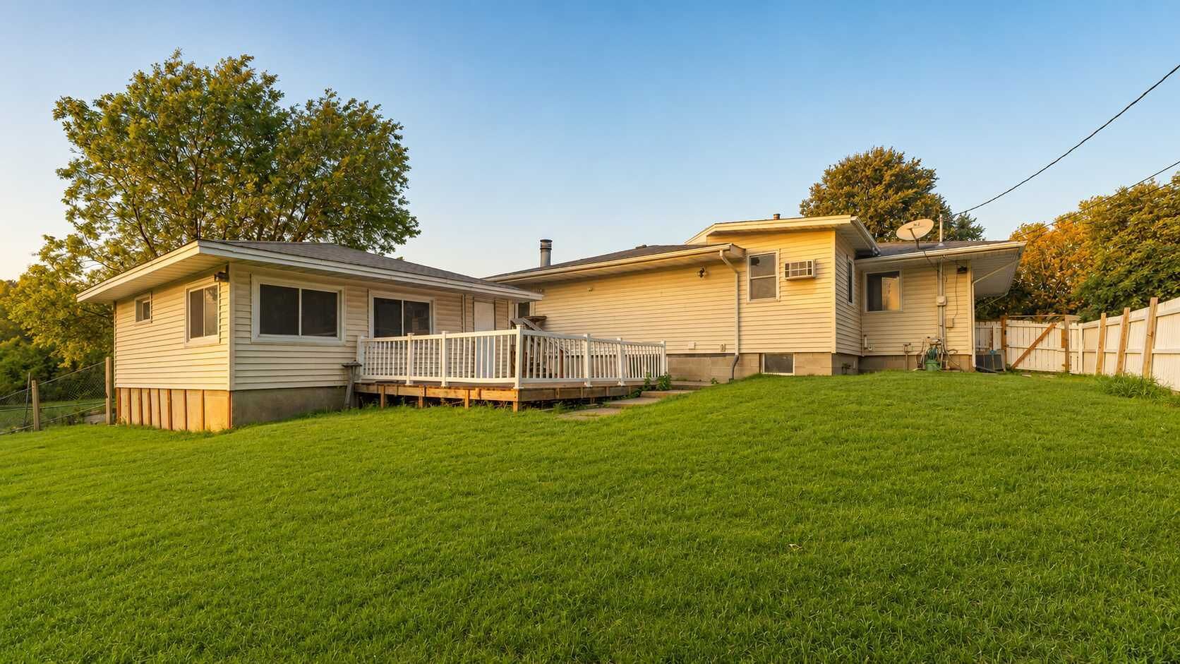 A two-story mobile home with a front deck and a fenced backyard.