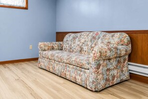 A room with a floral-patterned sofa against a light blue wall, wooden trim, and a wooden floor. - Spacious 7BR Brooklyn Center Home for 14 (Minneapolis)