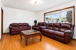 A living room with two leather sofas, a wooden coffee table, and a large window with a view of houses.