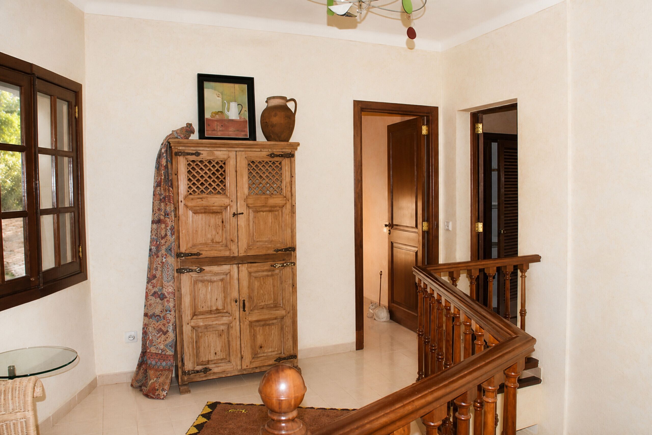 A wooden cabinet with a patterned cloth draped over it, a staircase with wooden balusters, and a door leading to another room.