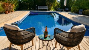 Ein Swimmingpool mit zwei Korbstühlen und einem Tisch, auf dem sich eine Flasche und ein Glas befinden.