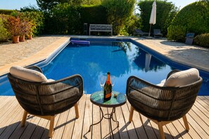 Ein Swimmingpool mit zwei Korbstühlen und einem Tisch, auf dem sich eine Flasche und ein Glas befinden.