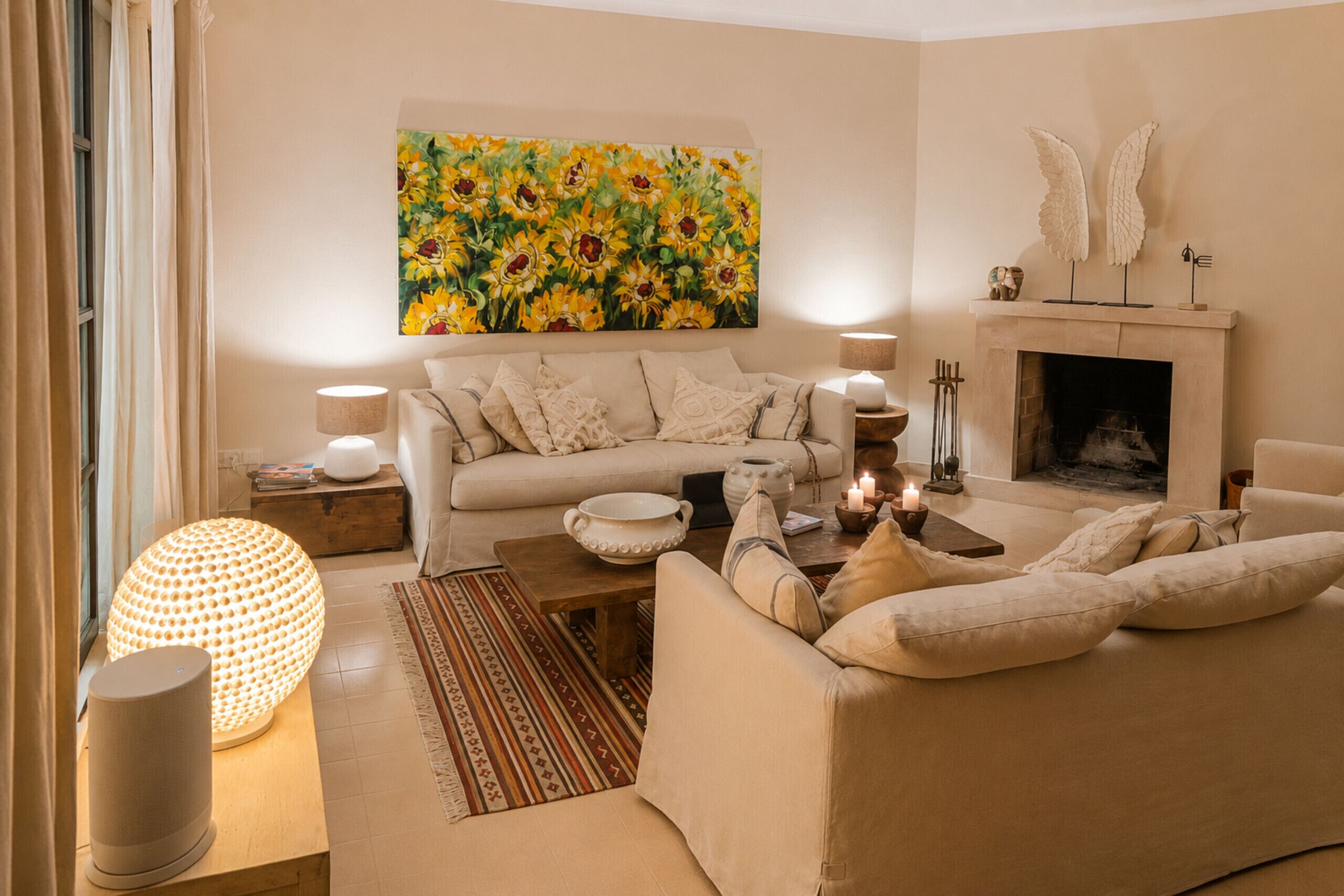 A cozy living room with a sofa set, a fireplace, and a large floral painting.