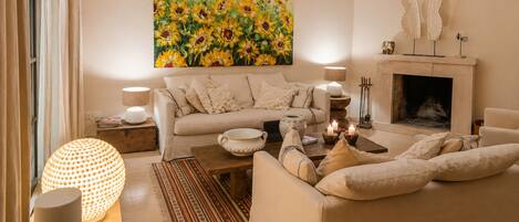 A cozy living room with a sofa set, a fireplace, and a large floral painting.