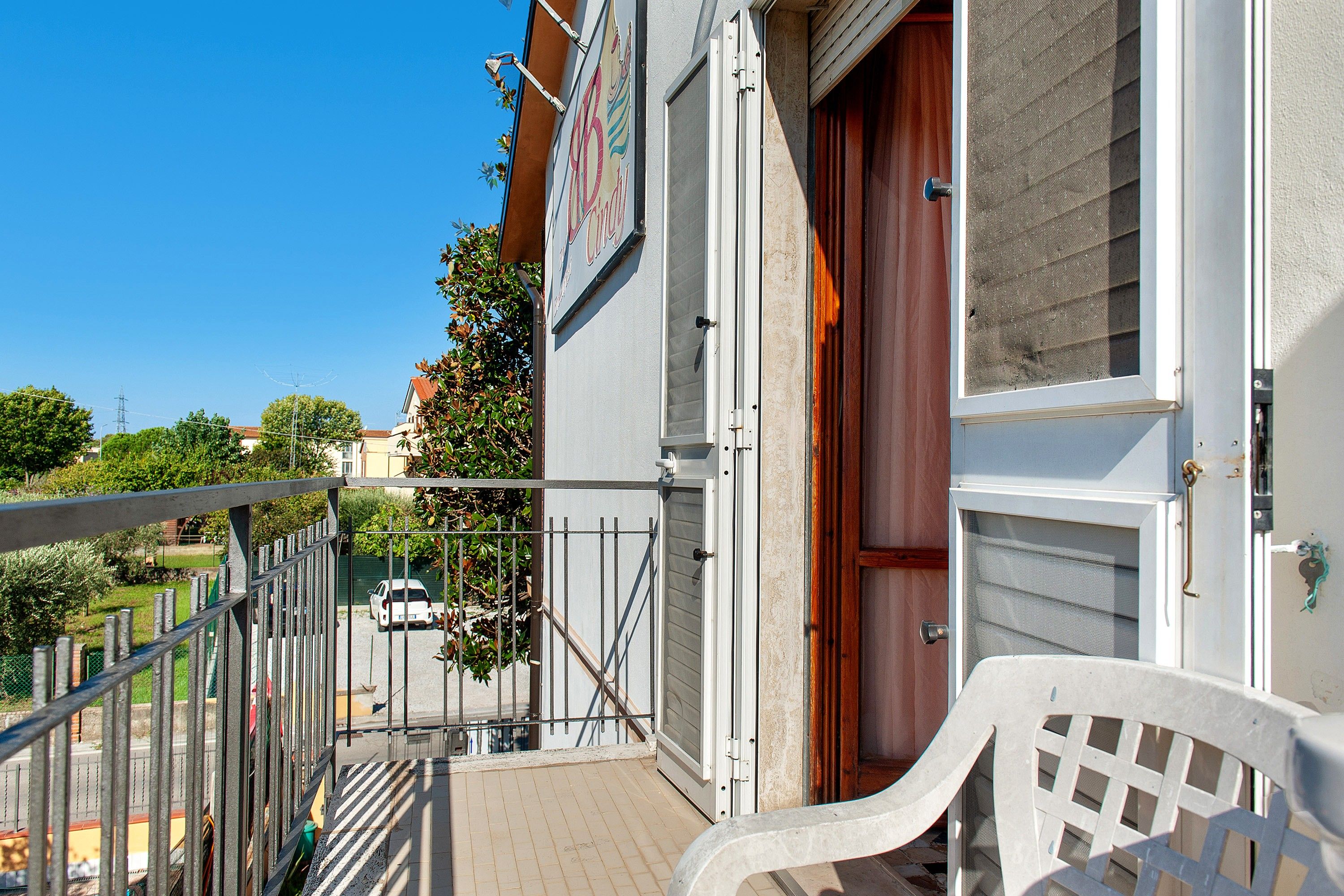 Un balcone con ringhiera in metallo, una porta in legno e una sedia bianca in plastica.