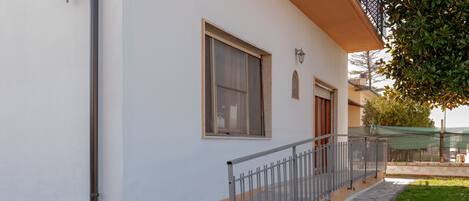 Un edificio con fachada blanca, barandilla metálica y un camino empedrado.
