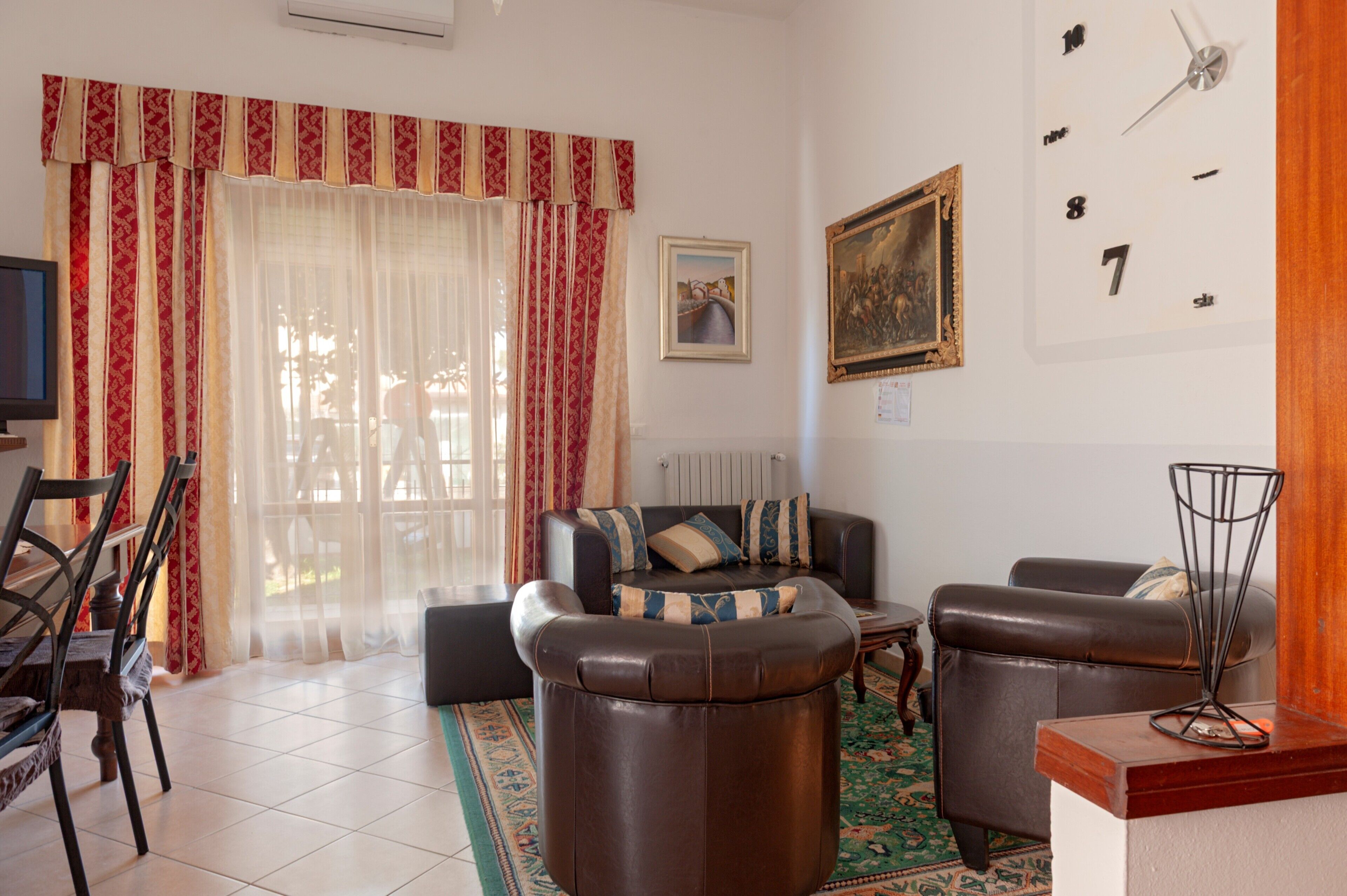 Ein Wohnzimmer mit Sofa, Sesseln, einem Fernseher und einem Bild an der Wand.