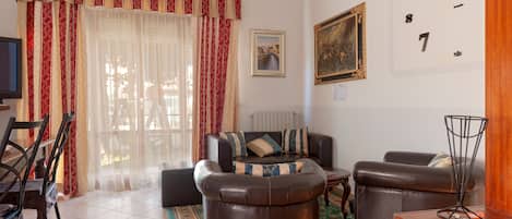 A living room with a sofa, chairs, a TV, and a painting on the wall.