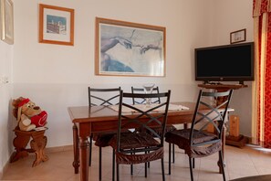 Ein Essbereich mit einem Holztisch, zwei Stühlen, einem Fernseher auf einem Schrank und einem gerahmten Kunstwerk über dem Tisch.