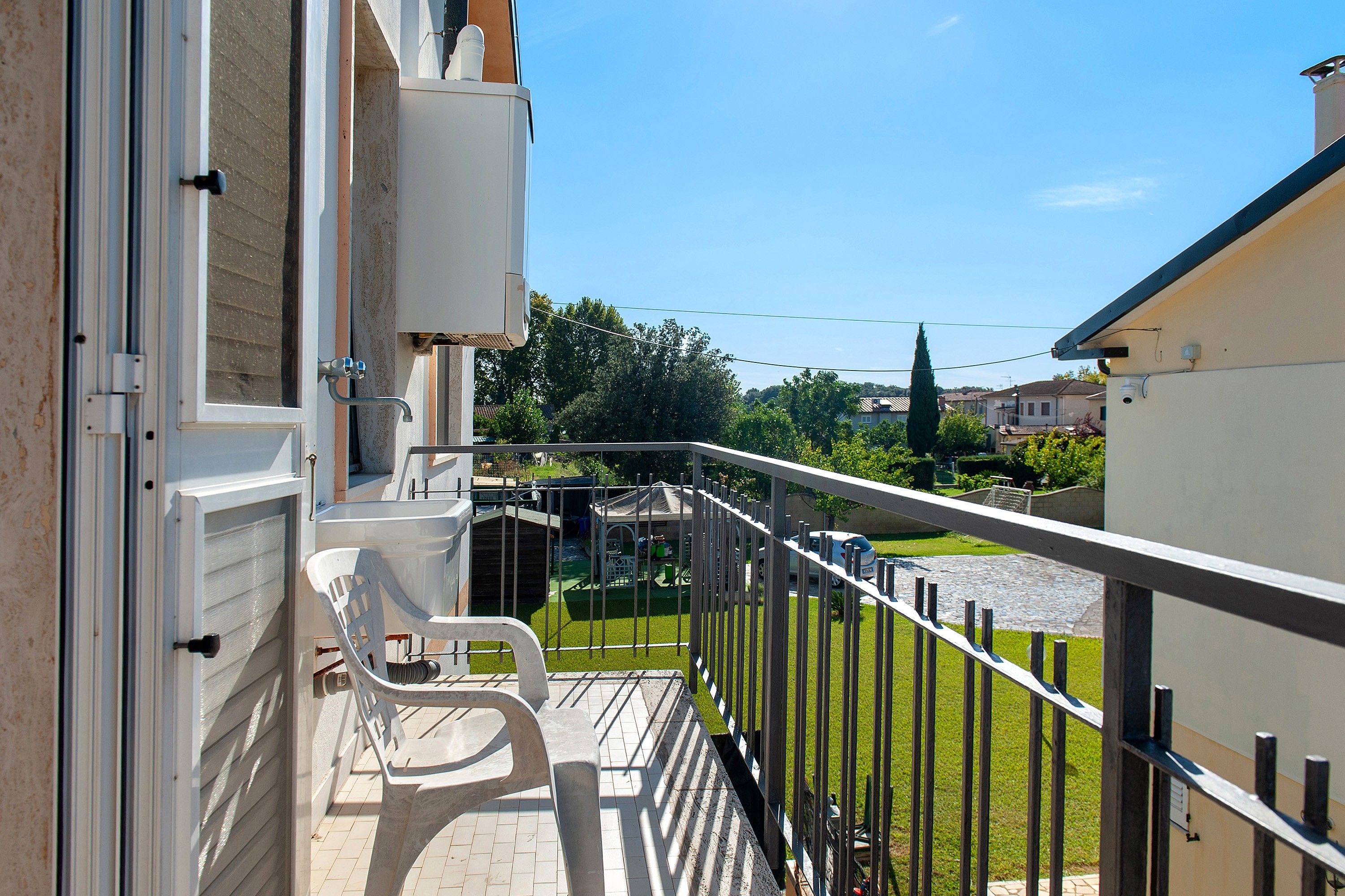 Un balcon avec une chaise, une petite table et une vue sur une pelouse verdoyante et des maisons au loin.