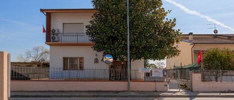 A two-story building with a balcony, a tree in front, and a clear sky.