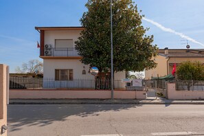 Un edificio a due piani con un balcone, un albero di fronte e cielo sereno.