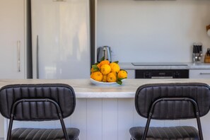 A modern kitchen with a white countertop, two black upholstered chairs, and a bowl of oranges. - Beautifully renovated three-bedroom holiday home sleeping 4 adults and 2 kids (Waiheke Island)