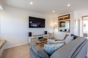 A modern living room with a flat-screen TV mounted on the wall, a wooden coffee table, a sofa with patterned cushions, and a floor lamp. - Beautifully renovated three-bedroom holiday home sleeping 4 adults and 2 kids (Waiheke Island)