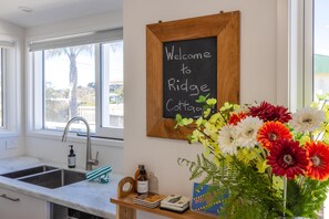 A kitchen with a sink, a wooden shelf with a chalkboard sign, and a vase of flowers. - Beautifully renovated three-bedroom holiday home sleeping 4 adults and 2 kids (Waiheke Island)