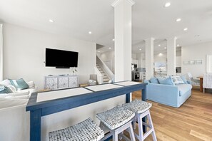 Ein modernes Wohnzimmer mit Fernseher, einer Bar mit Hockern, einem blauen Sofa und einer Treppe, die zur Küche führt.