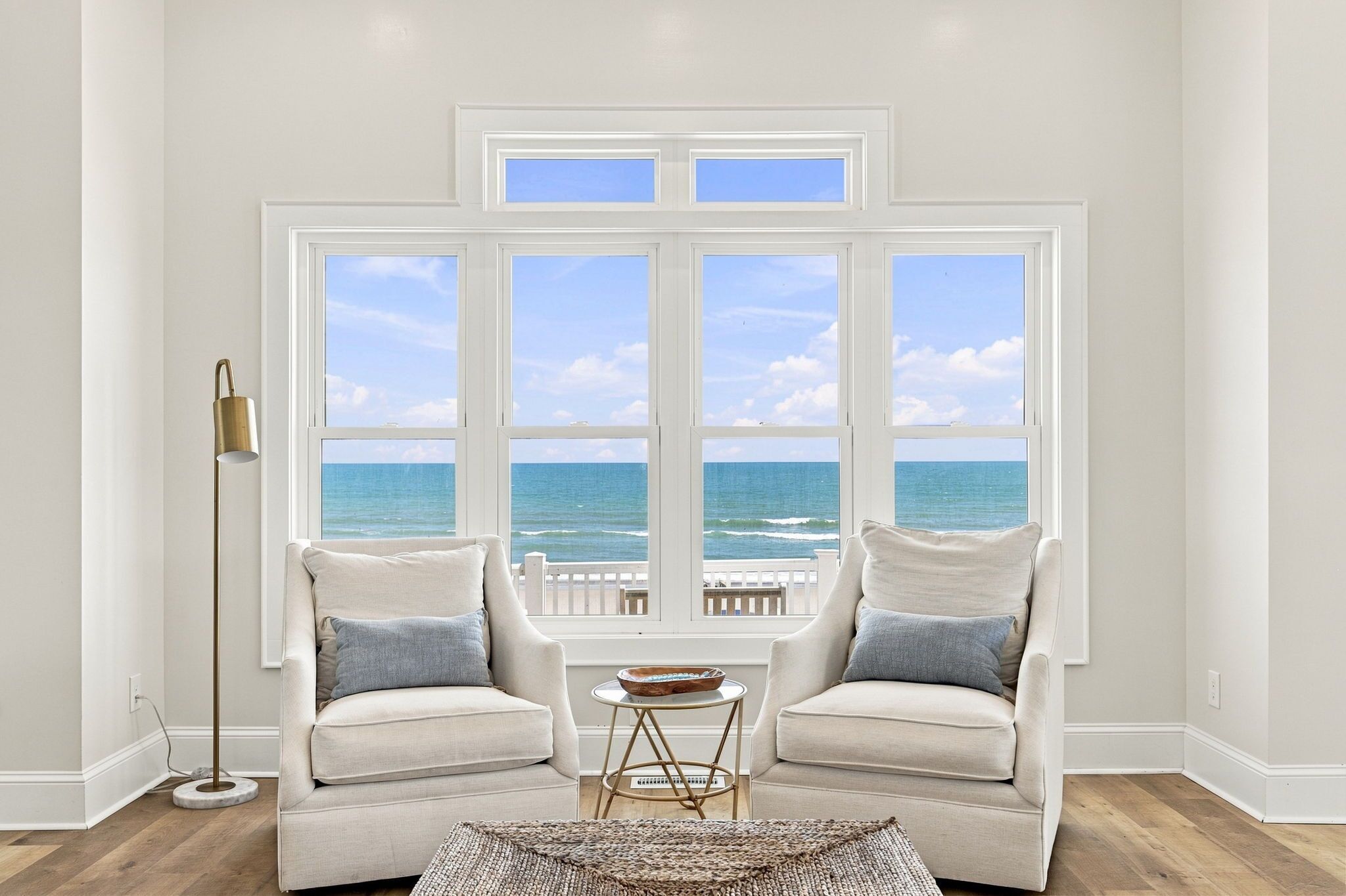Une pièce dotée d’une grande fenêtre donnant sur la mer, de deux fauteuils, d’une petite table ronde et d’un lampadaire.