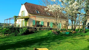 A stone house with green shutters, a garden with a wheelbarrow, and a clear blue sky. - Charming bed and breakfast with swimming pool in Dordogne (Plazac)