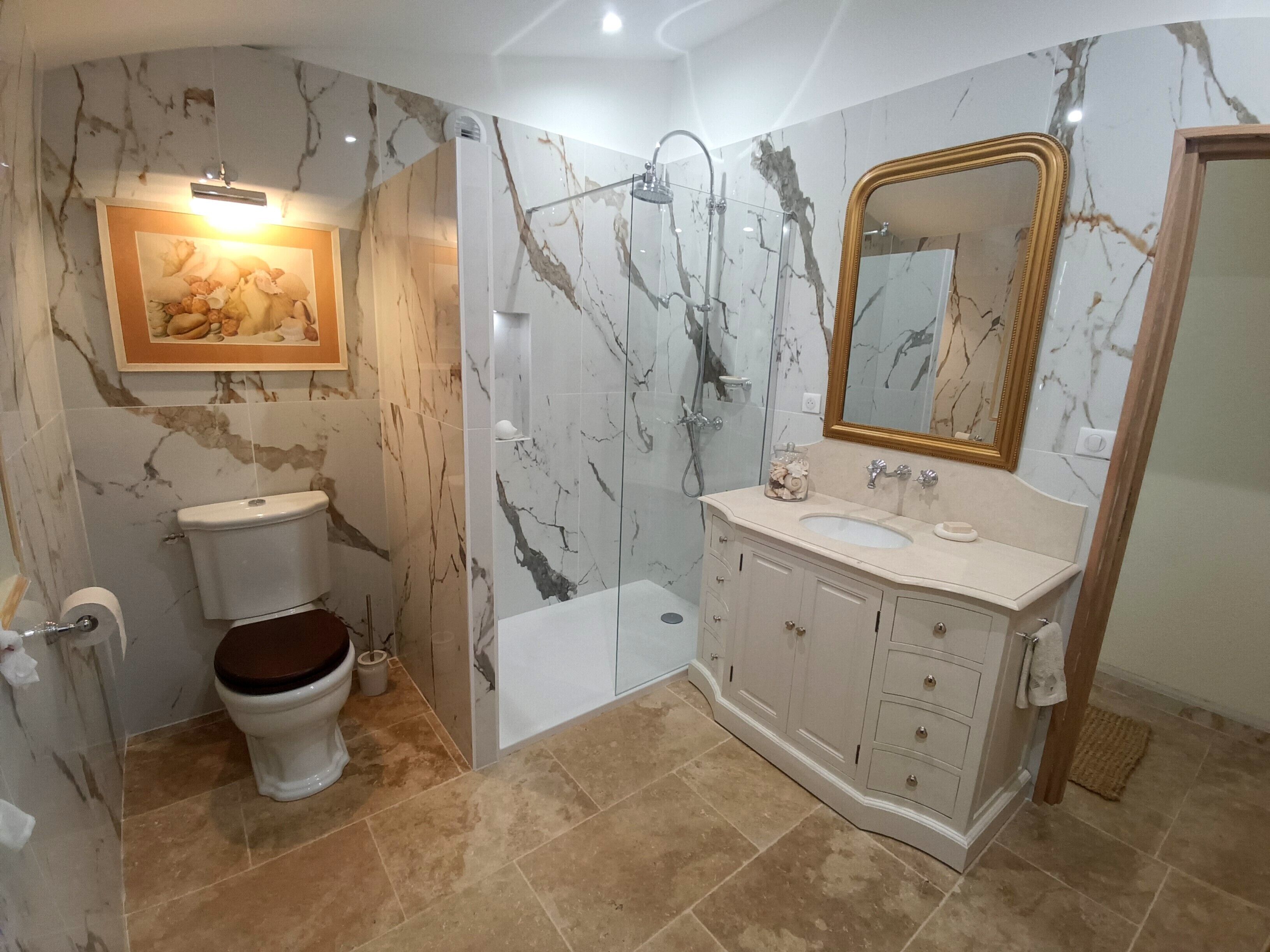 Une salle de bain comprenant des toilettes, un lavabo, une douche, des murs en marbre et un miroir.