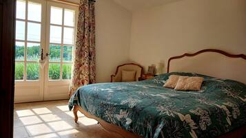 Ein Schlafzimmer mit Bett, einem Vorhangfenster, einer Kristallleuchtre und Blick auf Grün.