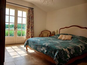 A bedroom with a bed, a window with curtains, a chandelier, and a view of greenery outside. - Charming bed and breakfast with swimming pool in Dordogne (Plazac)