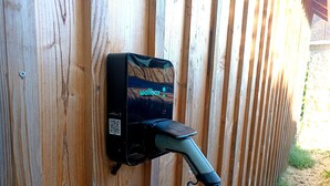 A wall-mounted wallbox with a QR code and a charging cable plugged in. - Charming bed and breakfast with swimming pool in Dordogne (Plazac)