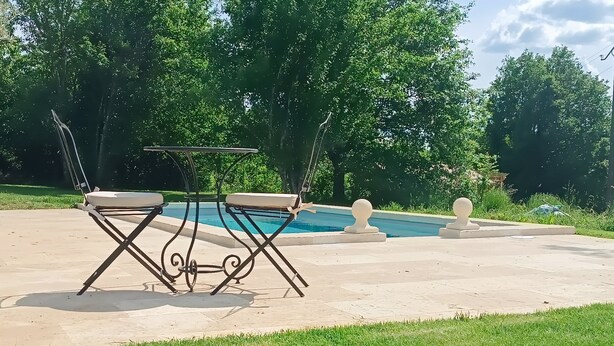 A poolside area with a metal table and chairs, surrounded by grass and trees. - Charming bed and breakfast with swimming pool in Dordogne (Plazac)
