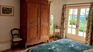 A bedroom with a large wooden wardrobe, a bed with a floral bedspread, a chair, a dresser, a mirror, and a window with curtains. - Charming bed and breakfast with swimming pool in Dordogne (Plazac)