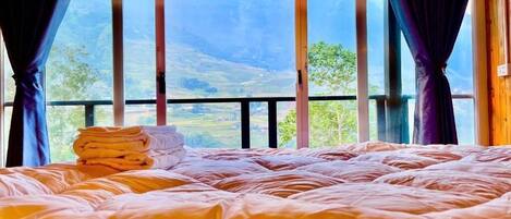Cama com vista para uma paisagem montanhosa através de grandes janelas.