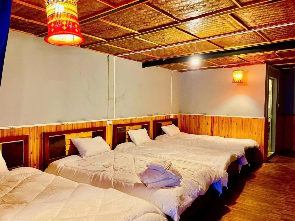 Een hotelkamer met drie bedden, houten hoofdeinden en een geweven plafond.
