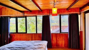 A room with a bed, wooden walls, large windows, and a hanging light fixture.