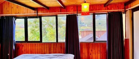 Una habitación con una cama, paredes de madera, ventanas amplias y una lámpara colgante.