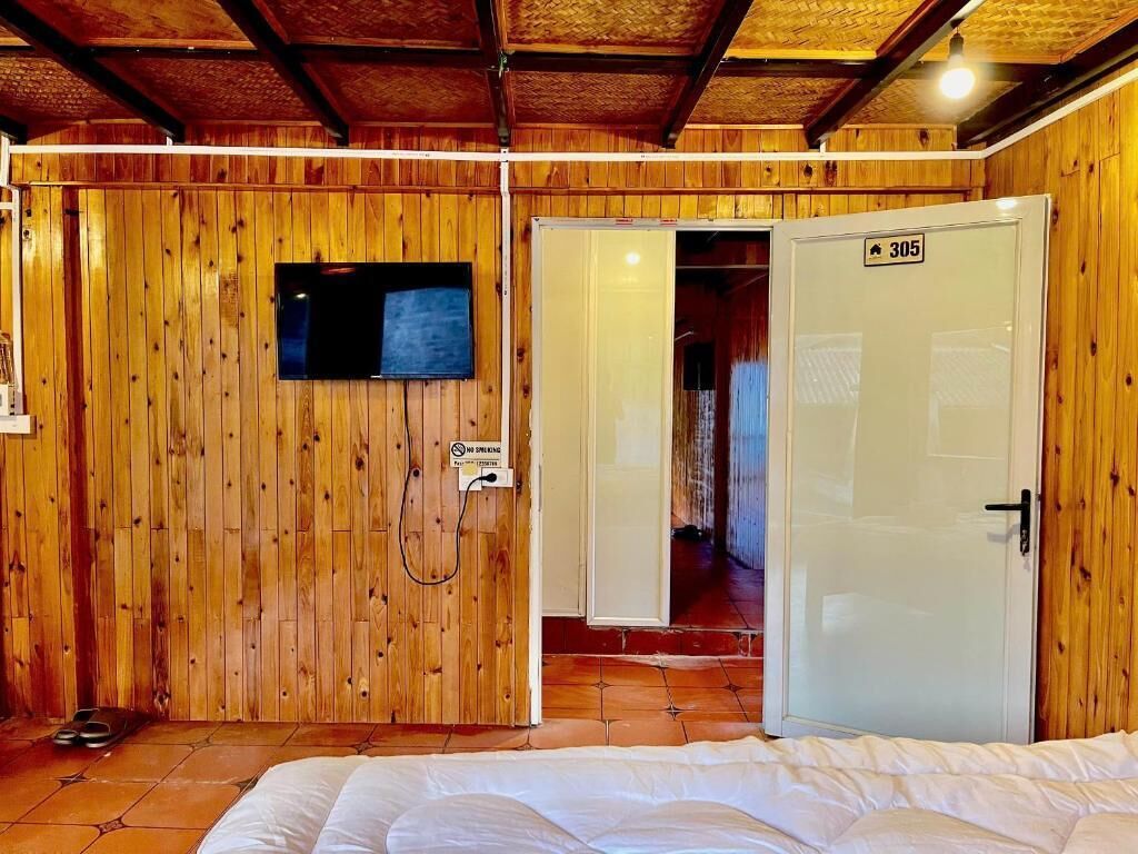 A wooden-paneled room with a bed, a television, and a door marked with the number 305.