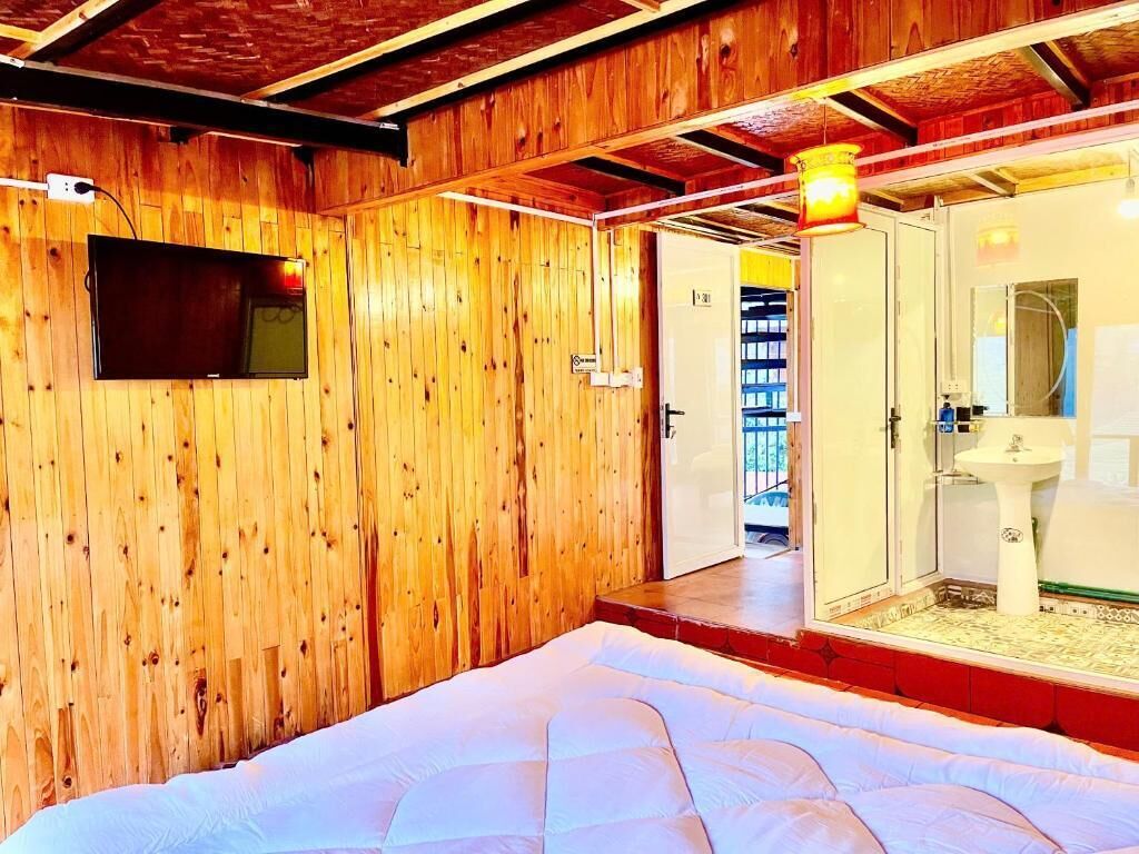 A room with wooden walls, a bed, a television, and a bathroom with a sink and mirror.
