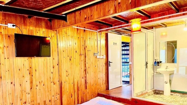 Una habitación con paredes de madera, una cama, un televisor y un baño con lavamanos y espejo.