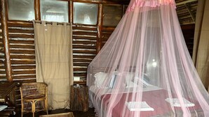 A rustic room with a bed under a pink canopy, a wicker chair, and a wooden nightstand. - Aaranyakam  (Vythiri)
