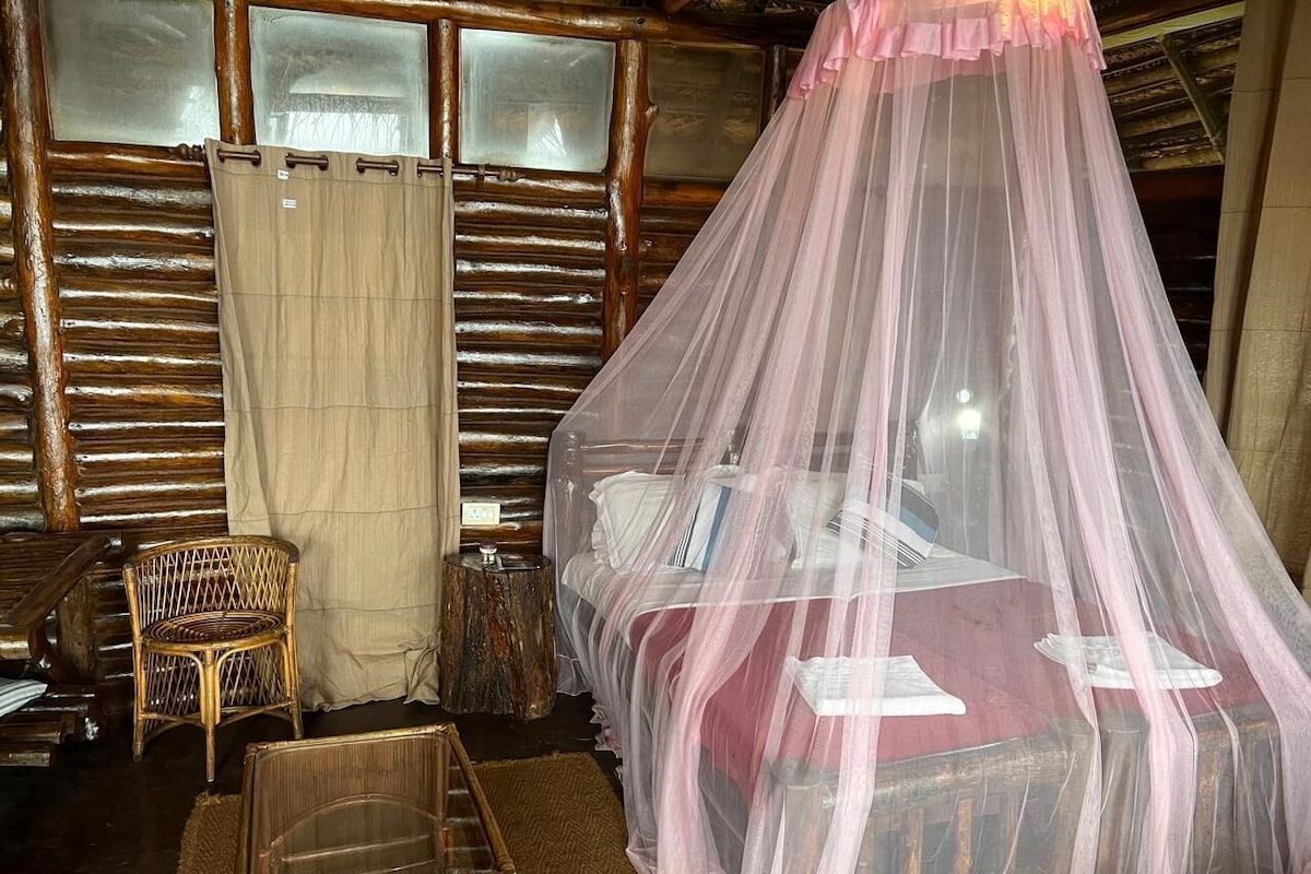 Une chambre rustique avec un lit placé sous un dais rose, une chaise en osier et une table de chevet en bois.