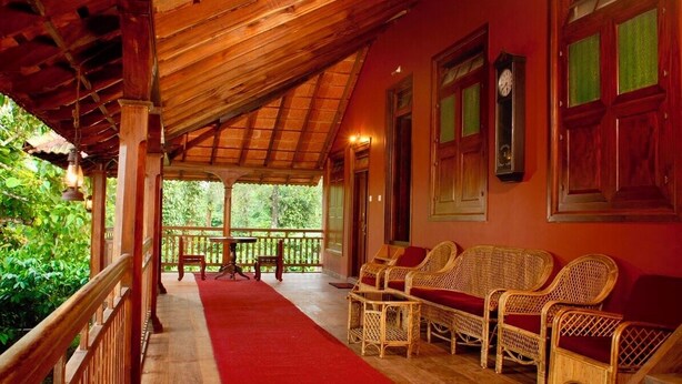 A covered outdoor seating area with wicker furniture and a red carpet. - Aaranyakam  (Vythiri)