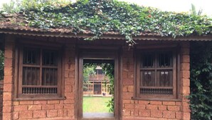 A rustic building with a brick facade, two windows with wooden frames, and a stone base. - Aaranyakam  (Vythiri)