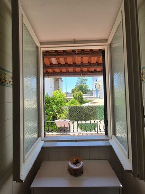 Ein Zimmer mit Fensterblick auf einen Garten, einem kleinen Tisch und einem Fliesenboden.