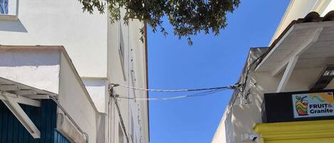 Una calle estrecha flanqueada por edificios, una persiana cerrada a la derecha y un letrero que dice 'FRUIT & Granite' a la izquierda.