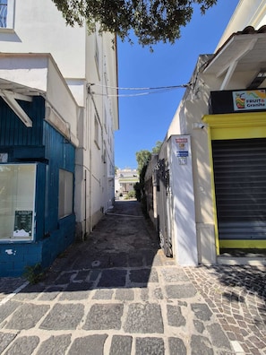 Eine schmale Gasse mit Gebäuden an beiden Seiten, ein geschlossener Rollladen rechts und ein Schild für 'FRUIT & Granite' links.