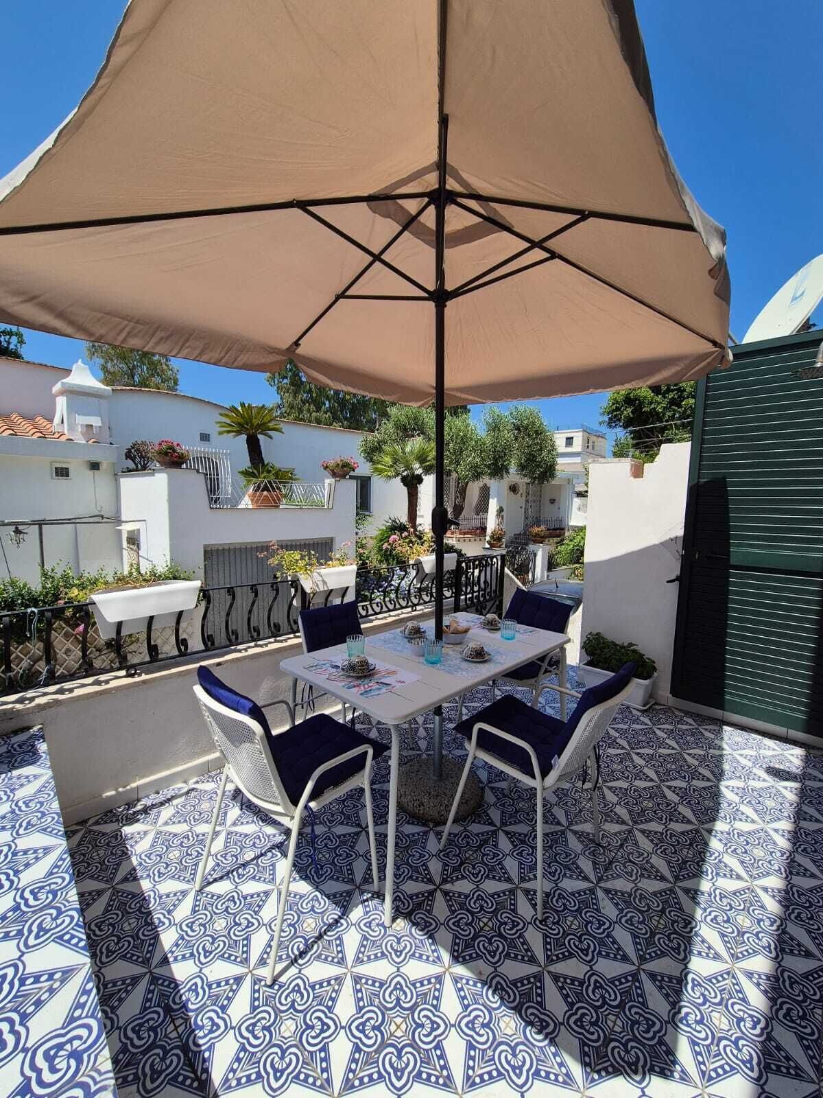 An outdoor patio with a table and chairs, a large umbrella, and patterned floor tiles.