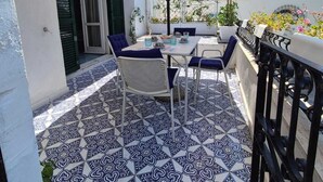 An outdoor patio with a table and chairs, a beige umbrella, and patterned floor tiles. - Apple Cake House - Sweet Silvana (Ischia)