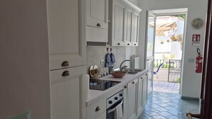 A kitchen with white cabinets, a stove, and a sink. There is a tiled floor and a view of the outside. - Apple Cake House - Sweet Silvana (Ischia)