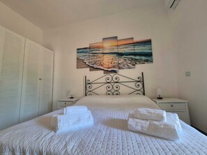 Ein Schlafzimmer mit einem Bett, einem an der Wand hängenden Bild einer Strandansicht, einem Kleiderschrank und Nachttischen.
