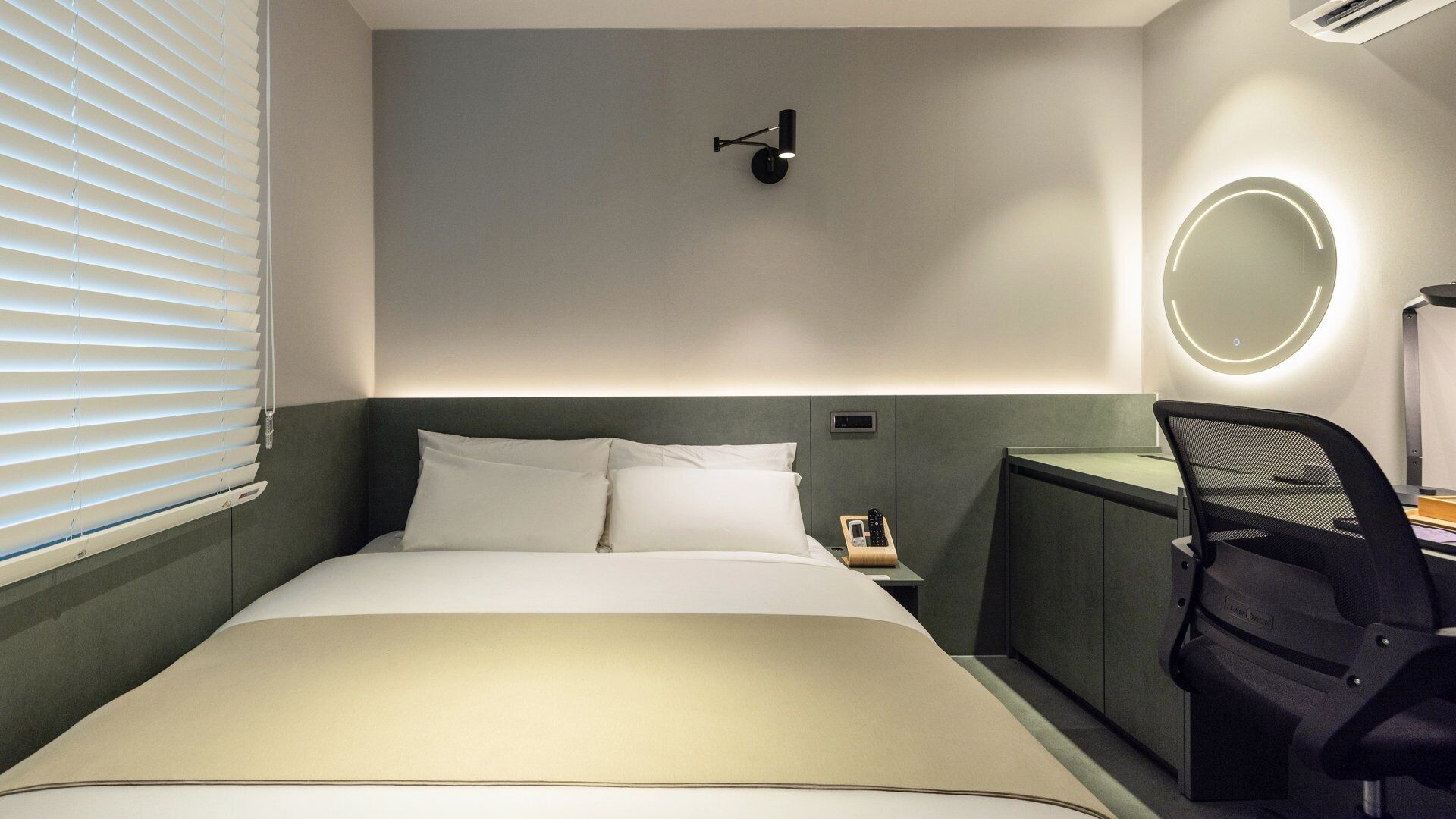 A hotel room with a bed, bedside table, lamp, and a chair.