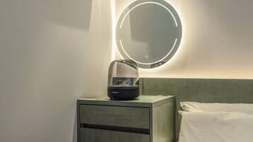Quarto de hotel com mesa de cabeceira, secador de cabelo e espelho com luz circular na parede.